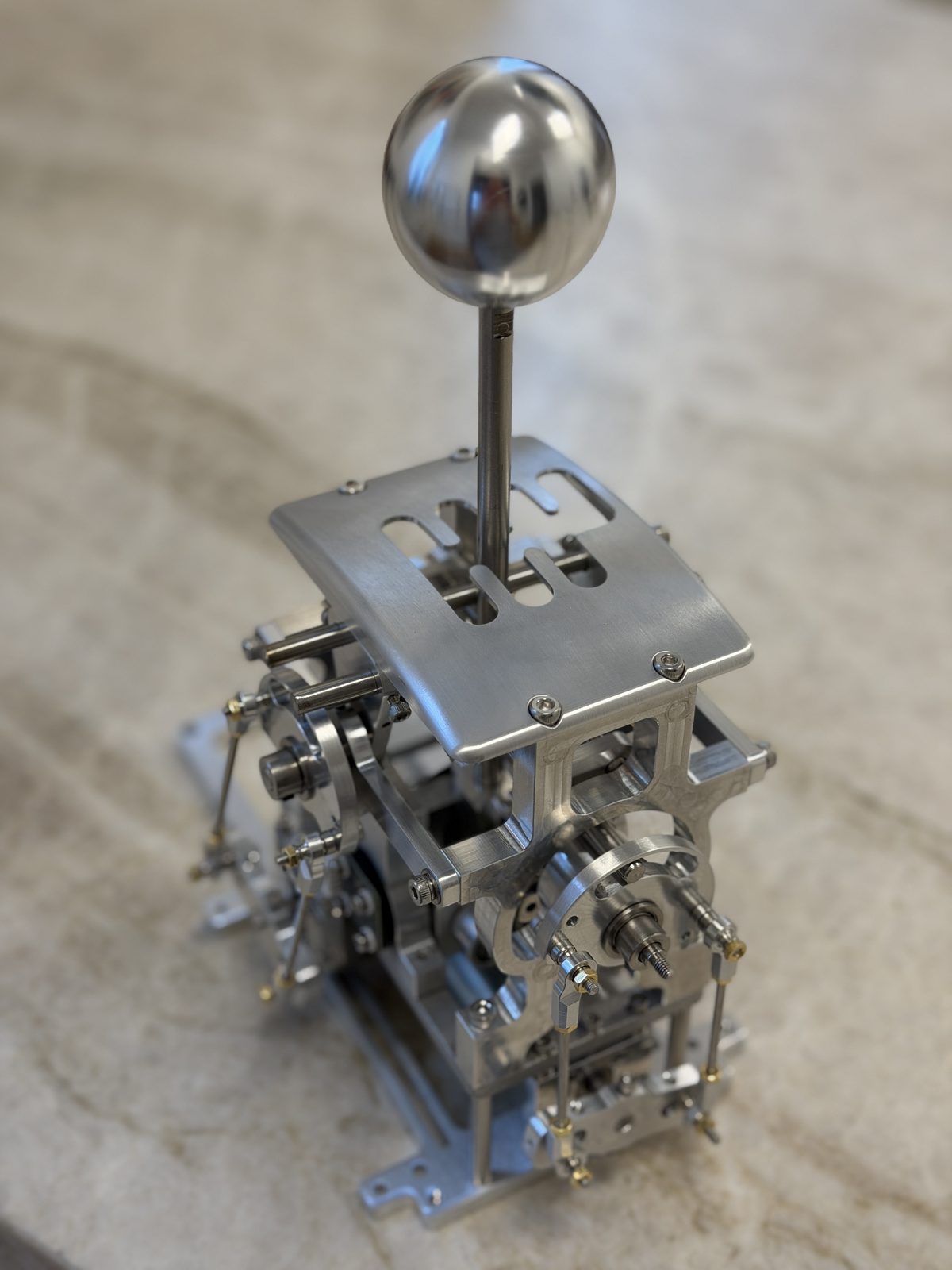 The bare H-gate mechanism: polished ball knob, brushed aluminium gate plate, and exposed electromechanical linkages below.
